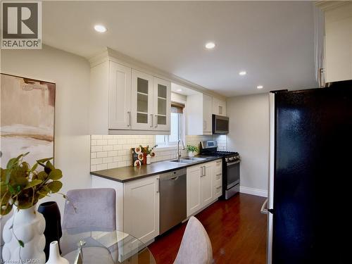 Kitchen featuring white cabinetry with glass-panel upper doors, dark countertops, white subway tile backsplash, recessed ceiling lighting, and wood-finish flooring - 449 Exmoor Street, Waterloo, ON 