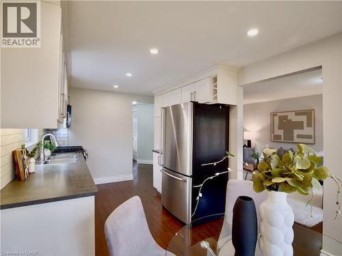 Kitchen featuring white cabinetry, wood-finish flooring, recessed lighting, stainless steel refrigerator, and dual-basin sink with tile backsplash - 449 Exmoor Street, Waterloo, ON 