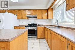 Kitchen featuring wood cabinetry, stainless steel gas range, coordinating stainless steel range hood, double basin stainless steel sink, and light-tone tile flooring - 