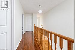 Hallway featuring wood-finish flooring, a traditional wood-finish railing with turned balusters, and a textured globe pendant light - 