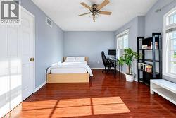 Bedroom featuring high-gloss wood-finish flooring, multi-pane windows, and a ceiling-mounted fan with integrated light fixture - 