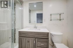 Bathroom featuring a wood-finish vanity with a stone-composite countertop, a glass-enclosed shower with a rainfall showerhead and mosaic tile inlay, a framed wall mirror, and dual glass wall-mounted s - 