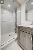 Walk-in glass shower with vertical mosaic accent tile, wood-finish vanity cabinet, solid-surface countertop with integrated sink, and framed wall-mounted mirror - 