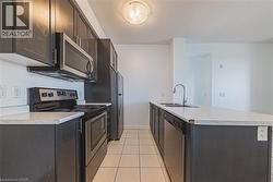 Kitchen featuring dark cabinetry, stainless steel appliances, light-toned countertops, a dual-basin sink, and tile flooring - 