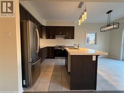 Kitchen featuring dark wood cabinetry, white tile backsplash, a center island with a solid surface countertop, stainless steel appliances, and pendant lighting - 