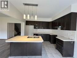 Kitchen featuring dark-finish cabinetry, white subway tile backsplash, center island with an integrated stainless steel sink, and a multi-light pendant fixture - 