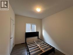 Room featuring wood-finish flooring, a neutral wall palette, an arched-panel interior door, a window with horizontal blinds, and a flush-mount ceiling light fixture - 