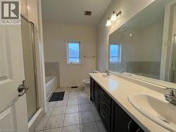 Double vanity with stone-finish countertop, dark wood cabinetry, glass-enclosed shower, soaking tub, and large wall-to-wall mirror - 