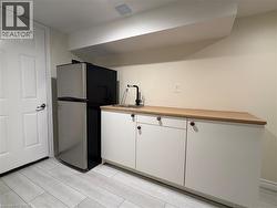 Wet bar area featuring white cabinetry, light-toned wood-finish countertop, stainless steel drop-in sink with a matte black faucet, and wood-finish tile flooring - 