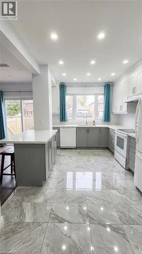 Kitchen featuring grey lower cabinetry, white upper cabinetry, white stone-finish countertops, a central island with bar seating, and large-format veined tile flooring - 1394 Cannon Street E, Hamilton, ON 