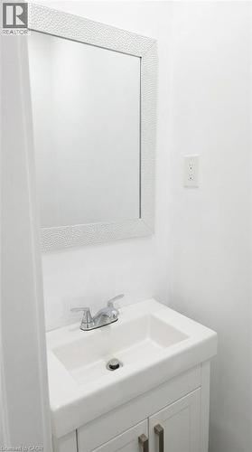Wall-mounted mirror with a textured frame, white vanity cabinet, rectangular basin, and dual-handle chrome faucet - 1394 Cannon Street E, Hamilton, ON 