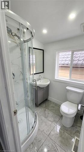 Corner glass shower enclosure with marbled wall surround, pedestal sink with integrated cabinet, large-format tile flooring, and recessed ceiling lighting - 1394 Cannon Street E, Hamilton, ON 