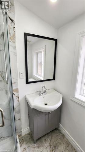 Bathroom vanity featuring a grey cabinet, white ceramic sink, polished chrome faucet, and black-framed wall mirror, complemented by tile flooring and stone-patterned shower surround - 1394 Cannon Street E, Hamilton, ON 