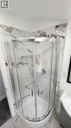 Corner shower featuring a curved glass enclosure, chrome hardware, and large-format wall tile with a veined pattern - 1394 Cannon Street E, Hamilton, ON 