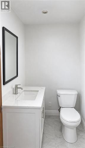 Vanity featuring a stone-surface countertop, rectangular undermount sink, brushed nickel faucet, and a wall-mounted mirror with a black frame, paired with a white porcelain toilet and stone-finish til - 1394 Cannon Street E, Hamilton, ON 