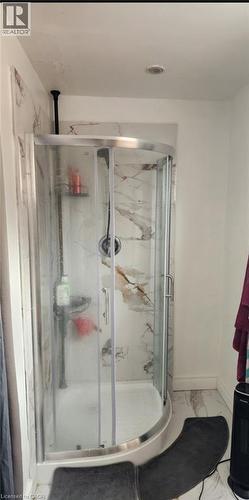 Corner shower enclosure featuring curved glass doors, a silver-tone finish frame, wall-mounted shower fixture, and surround panels with a natural veining pattern - 1394 Cannon Street E, Hamilton, ON 
