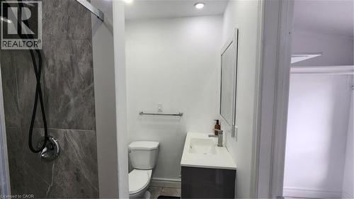 Shower enclosure featuring floor-to-ceiling stone-pattern tile and a modern rainfall showerhead, vanity with a white rectangular basin, stone-surface countertop, and a wall-mounted framed mirror - 1394 Cannon Street E, Hamilton, ON 