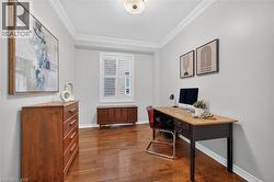 Room featuring polished wood-finish flooring, crown molding, a central ceiling-mounted light fixture, and a window with plantation-style shutters - 