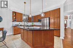 Kitchen featuring custom wood cabinetry, dark stone countertops, an expansive center island with a built-in sink, stainless steel appliances, and glass pendant lighting - 