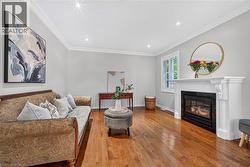 Elegant living room showcasing gleaming hardwood flooring, a gas fireplace with white mantel surround, and recessed ceiling lighting - 