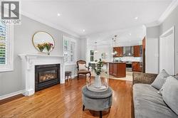 Fireplace with ornate white mantel and dark stone surround, wood-finish flooring, crown molding, plantation shutters, and kitchen with central island - 