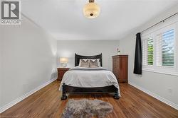 Bedroom featuring wood-finish flooring, a neutral color palette, and a window with plantation-style shutters - 