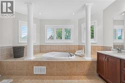 Soaking tub set in a tiled platform with dual architectural columns, plantation shutters, and recessed lighting - 