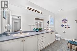 Double vanity featuring white cabinetry, dual undermount sinks, solid-surface countertops, full-width wall mirror, and integrated multi-bulb vanity lighting - 