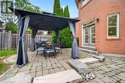 Rear exterior featuring a red brick facade, stone-paver patio, natural stone tiered hardscaping, and a fixed metal-frame gazebo - 