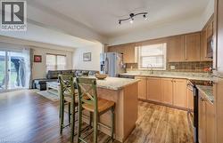Kitchen featuring light-finish cabinetry, stone-patterned countertops, wood-finish flooring, a central island, and stainless steel appliances - 