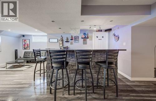 Built-in wet bar featuring stone-veneer facing, dark countertop, recessed ceiling lighting, and wood-finish flooring - 521 Snowdrop Court, Kitchener, ON 