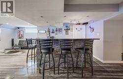 Built-in wet bar featuring stone-veneer facing, dark countertop, recessed ceiling lighting, and wood-finish flooring - 