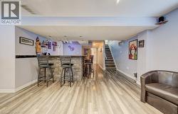 Custom built-in bar featuring a stacked-stone facade, dark countertop, recessed lighting, and wood-finish flooring - 