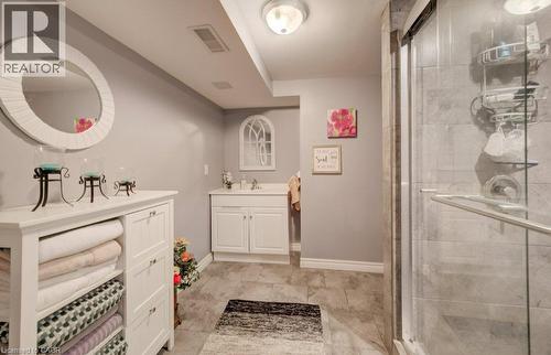 Bathroom featuring a white vanity cabinet, ceramic tile flooring, a glass-enclosed shower, and a circular wall-mounted mirror - 521 Snowdrop Court, Kitchener, ON 