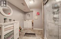 Bathroom featuring a white vanity cabinet, ceramic tile flooring, a glass-enclosed shower, and a circular wall-mounted mirror - 