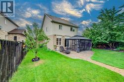Rear exterior featuring a brick and vinyl siding facade, stone-paver patio, metal-framed gazebo, and enclosed perimeter fencing - 