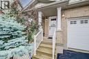 Exterior entrance featuring brick cladding, a covered porch with column supports, white railings, and a single-car garage with rectangular inset windows - 521 Snowdrop Court, Kitchener, ON 