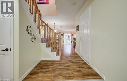 Foyer entry featuring wood-finish flooring, a staircase with a wooden balustrade, and a multi-panel door - 521 Snowdrop Court, Kitchener, ON 