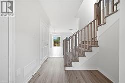 Entryway featuring wood-finish flooring, a staircase with wood-tone railing, carpeted treads, and paneled doors - 