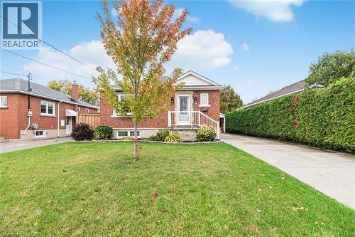 Red brick exterior featuring a white railed front porch, concrete driveway, and manicured front lawn - 43 Alderney Avenue, Hamilton, ON 