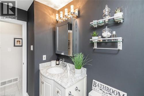 Vanity featuring a stone-composite countertop with an integrated basin, mirrored medicine cabinet, multi-bulb wall-mounted light fixture, and two wall-mounted glass shelves with metallic support brack - 43 Alderney Avenue, Hamilton, ON 