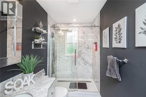 Walk-in shower enclosure featuring floor-to-ceiling stone-patterned tile, sliding glass door, and integrated recessed shelving, complemented by a stone-topped vanity and wall-mounted metal shelving - 43 Alderney Avenue, Hamilton, ON 