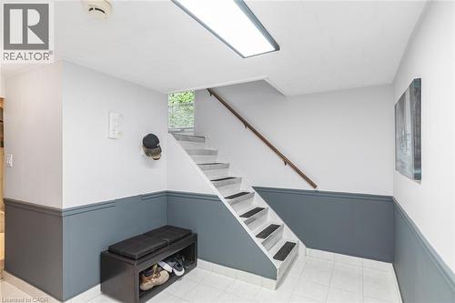 Staircase featuring a wooden handrail, tile flooring, and two-tone wall paneling - 43 Alderney Avenue, Hamilton, ON 
