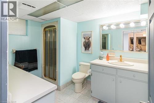 Bathroom featuring a vanity with integrated sink, brass-tone faucet, large wall-mounted mirror with integrated lighting, glass-enclosed shower, and tile flooring - 43 Alderney Avenue, Hamilton, ON 