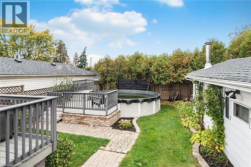 Backyard featuring a tiered wood-finish deck with railings, circular above-ground pool, stone-paver walkway, and manicured lawn - 43 Alderney Avenue, Hamilton, ON 