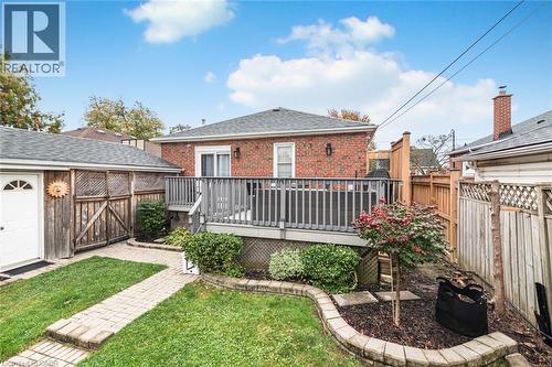 Red brick exterior featuring a raised wood deck, paved stone walkway, privacy fencing, and tiered stone garden edging - 43 Alderney Avenue, Hamilton, ON 