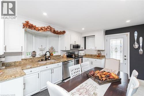 Kitchen featuring white cabinetry, stone countertops, stainless steel appliances, a double-basin sink with a matte black faucet, and a bay window - 43 Alderney Avenue, Hamilton, ON 