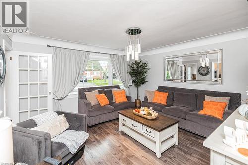 Living room featuring wood-finish flooring, a multi-light pendant fixture, a rectangular wall-mounted mirror, and a glass-paneled door - 43 Alderney Avenue, Hamilton, ON 