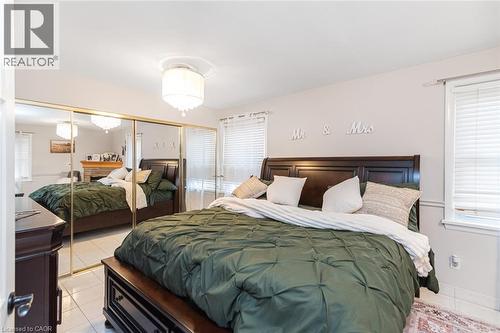Bedroom featuring polished tile flooring, wall-to-wall mirrored closet doors, dual windows with fitted blinds, and a drum-style ceiling light fixture - 43 Alderney Avenue, Hamilton, ON 