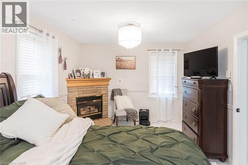 Corner fireplace with textured stone surround, wood mantel, and glass-front insert, complemented by chair rail molding, windows with horizontal blinds, and a drum-style ceiling light fixture - 43 Alderney Avenue, Hamilton, ON 